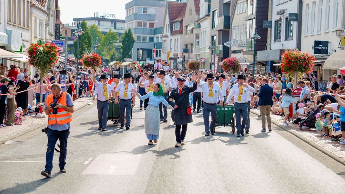 Die Symbolfiguren Jan und Libett in traditioneller Kleidung marschieren als Teil des Umzugs. Hinter ihnen befinden sich die Mitglieder des Marktausschusses in weißen Hemden